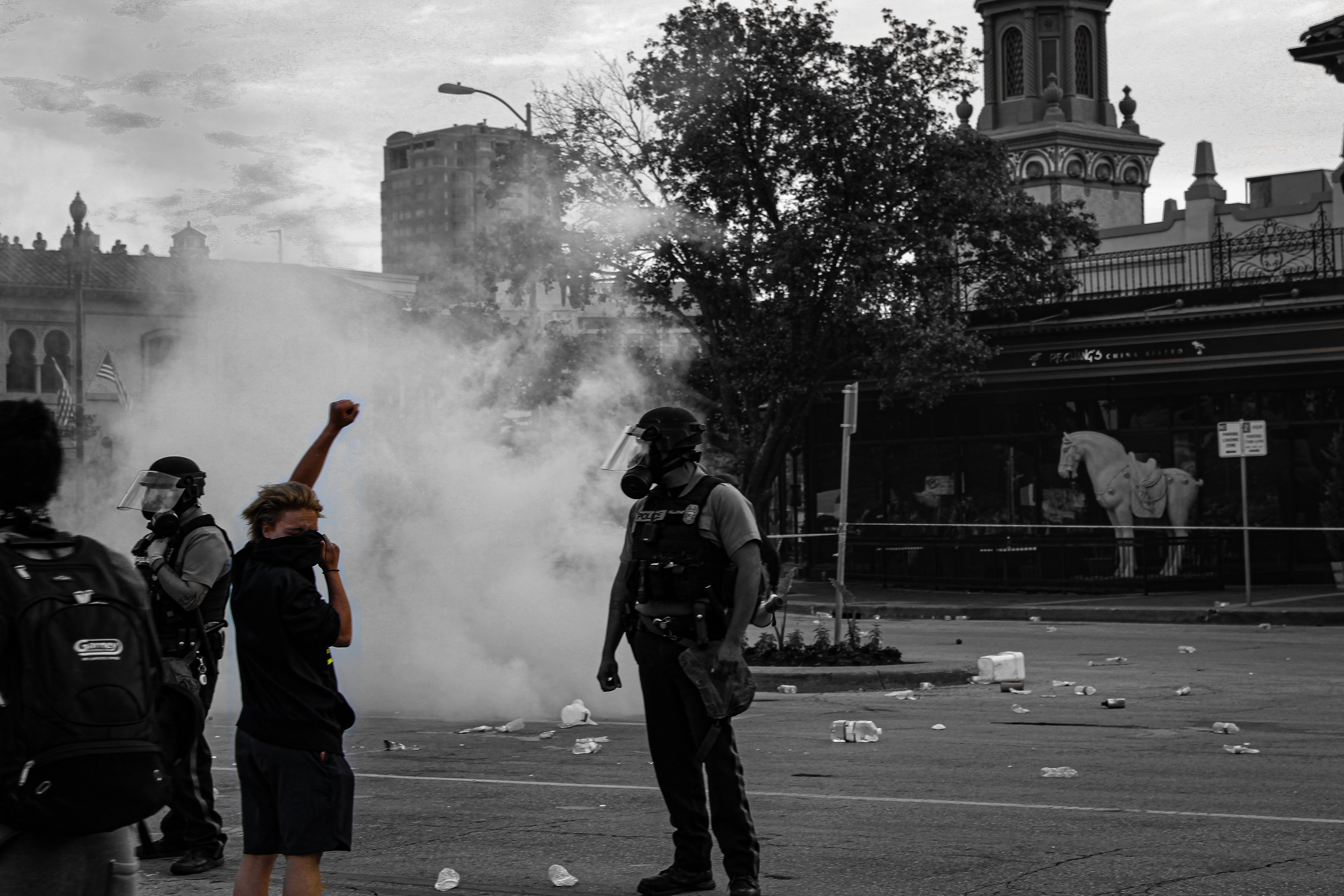 Police standing while a protester stands in tear gas with a fist raised